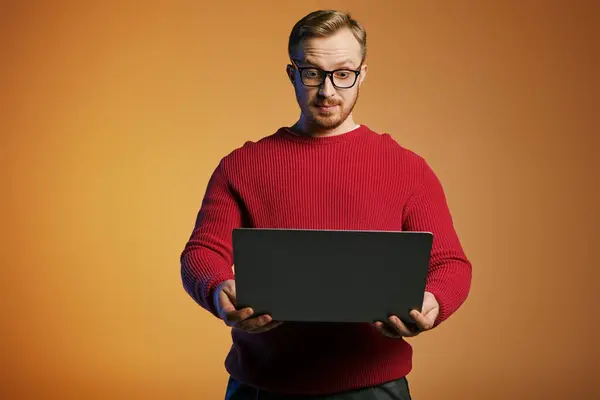 A handsome man in a red sweater holds a laptop, showcasing modern technology. — Stock Photo