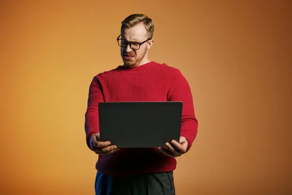 A fashionable man in a red sweater holds a laptop. — Stock Photo