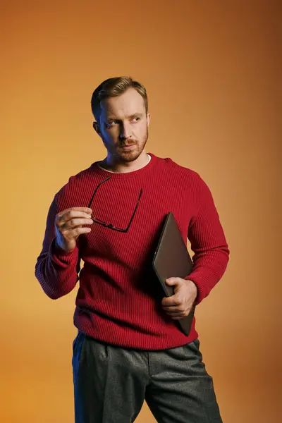 A stylish man in a red sweater actively holding a laptop. — Stock Photo