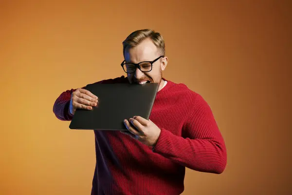 A stylish man dressed in a red sweater holding a laptop. — Stock Photo