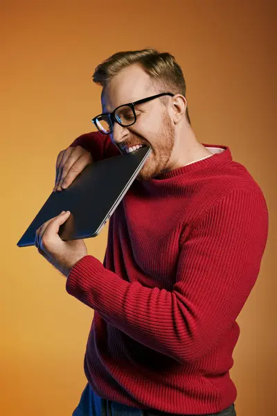 Un hombre con estilo en un suéter rojo sostiene un ordenador portátil en una pose cautivadora. - foto de stock