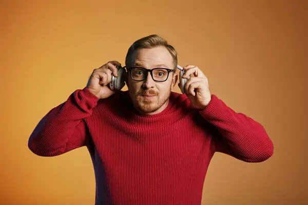 A handsome man in a red sweater holding a pair of glasses and headphones. — Stock Photo