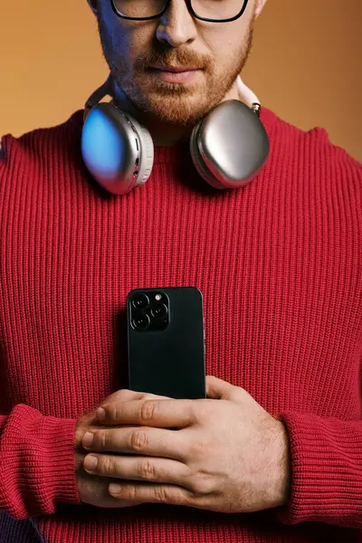 A man in stylish attire listens to music through headphones while holding a cell phone. — Stock Photo
