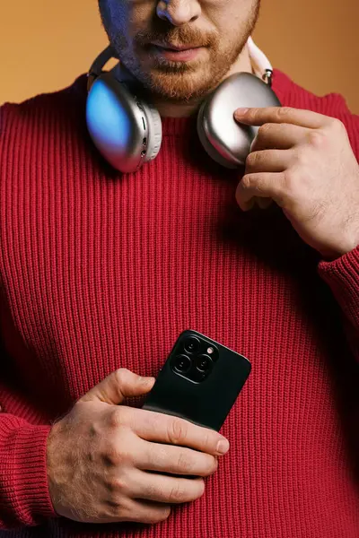 Handsome man in stylish attire listening to music on headphones while holding a cell phone. — Stock Photo