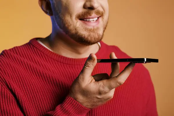 Handsome man actively posing in a red sweater, holding a black phone. — Stock Photo