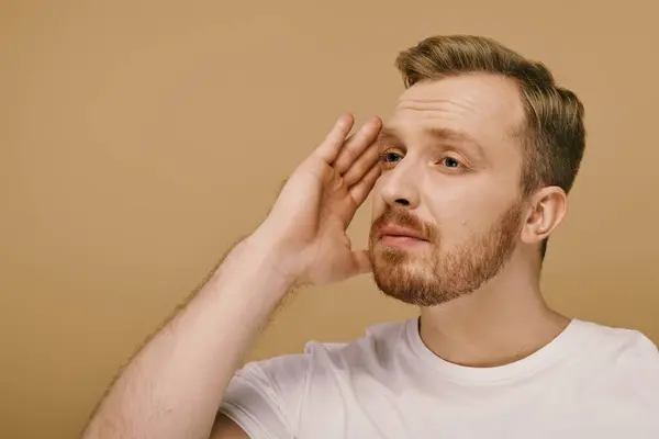 A stylishly dressed man with a beard places his hand on his face, contemplating deeply. — Stock Photo