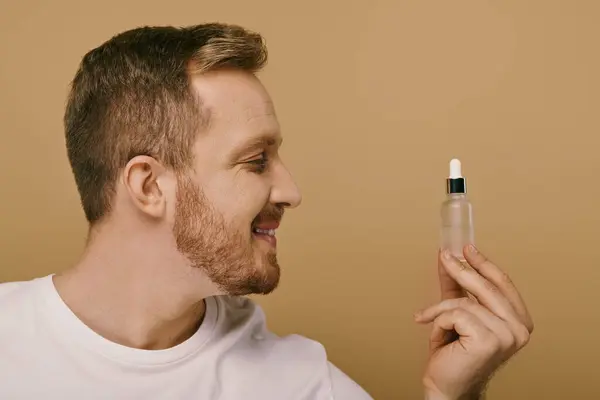Ein Mann in Freizeitkleidung hält eine Flasche Serum für seine Hautpflege in der Hand. — Stockfoto