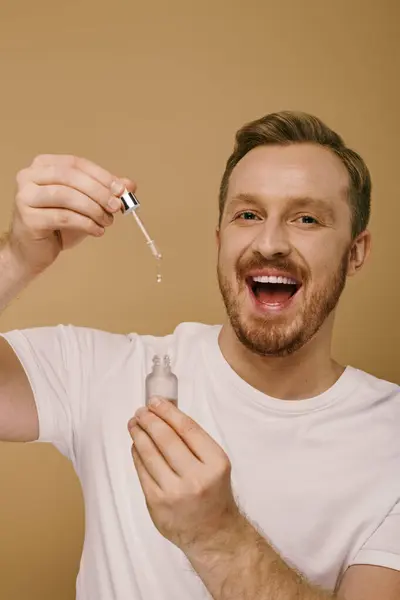 Handsome man in casual attire performs skin care routine with serum. — Stock Photo