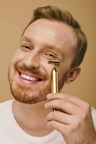 Un hombre elegante sonríe, sosteniendo el rodillo facial. - foto de stock