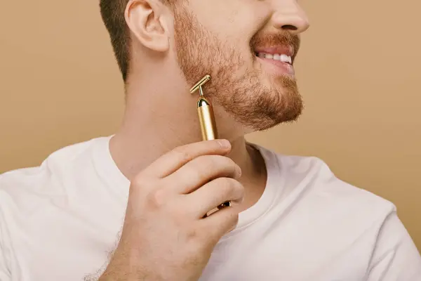 Handsome man in casual attire holds a shiny gold face roller in his hand. — Stock Photo