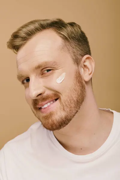 Ein gutaussehender Mann in lässiger Kleidung trägt fröhlich eine Gesichtscreme zur Hautpflege. — Stockfoto