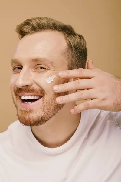 Un uomo in abbigliamento casual sta applicando felicemente la crema sul suo viso. — Foto stock