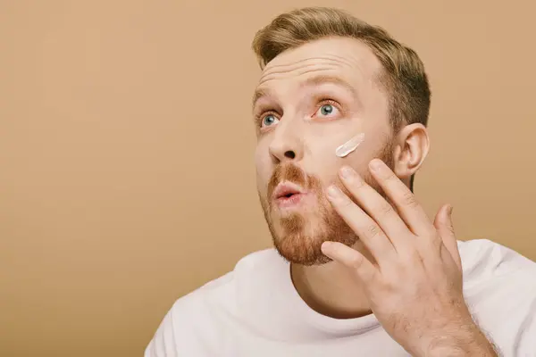 Schöner Mann in lässiger Kleidung, der für die Hautpflege eine Gesichtscreme aufträgt. — Stockfoto