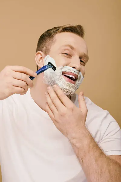 A man in casual attire shaving his face with a razor. — Stock Photo
