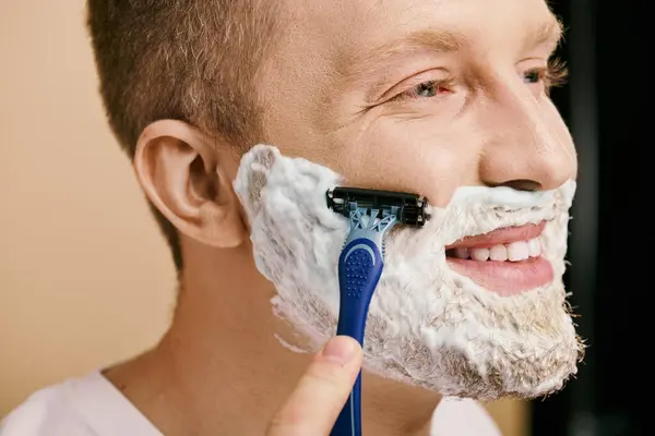 A man in casual attire carefully shaves his face with a razor. — Stock Photo