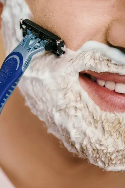 A man in casual attire shaving his face with a razor. — Stock Photo