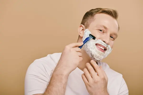 A suave man in casual attire performs his skincare routine, skillfully shaving his face with a razor. — Stock Photo