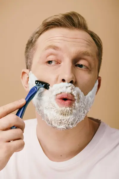 A man in casual attire shaving his face with a razor. — Stock Photo
