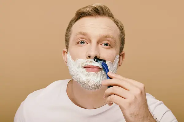 Un hombre con atuendo casual afeitándose cuidadosamente la cara con una navaja de afeitar. - foto de stock