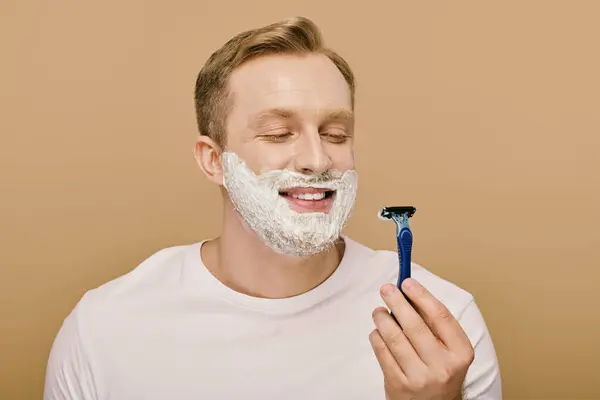 A man in casual attire shaving his face with a razor. — Stock Photo