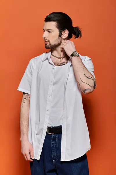 Handsome man with ponytail standing confidently against vibrant orange wall. — Stock Photo