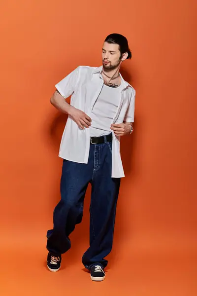 Stylish man standing against a vivid orange backdrop. — Stock Photo