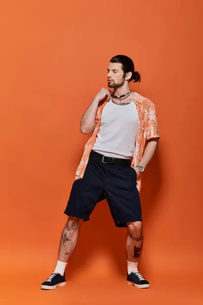 Hombre guapo en camisa blanca y pantalones cortos negros de pie con confianza delante de la pared naranja brillante. - foto de stock