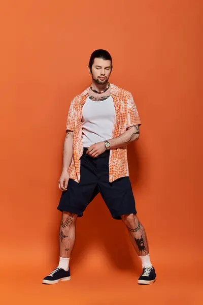 Schöner kaukasischer Mann in trendiger Kleidung steht selbstbewusst vor einer leuchtend orangen Wand. — Stockfoto