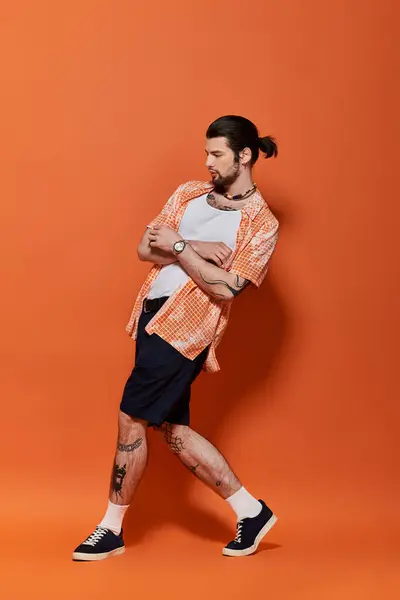 Stylish Caucasian man with tattoos posing against orange backdrop. — Stock Photo