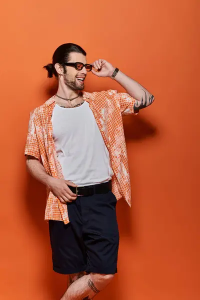 Handsome caucasian man in trendy attire standing confidently in front of a bright orange wall. — Stock Photo