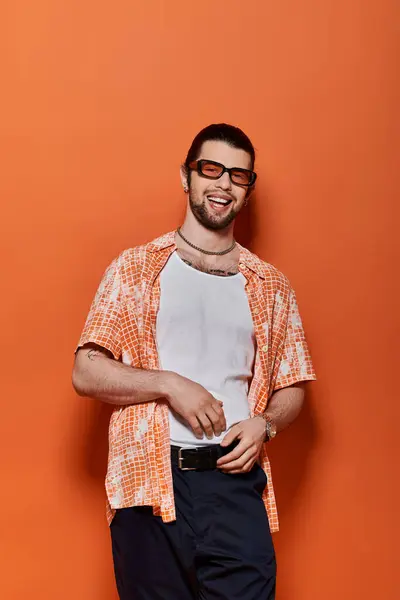 A stylish man with beard and glasses stands confidently in front of an orange wall. — Stock Photo