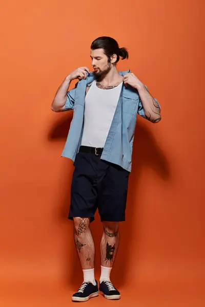 Bello uomo con tatuaggi in piedi in abito alla moda contro sfondo arancione brillante. — Foto stock