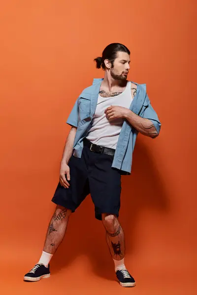 Fashionable man with goatee stands boldly in front of vivid orange backdrop. — Stock Photo