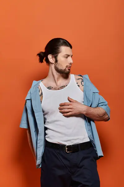 Caucasian man with arm tattoo standing stylishly in front of vibrant orange wall. — Stock Photo