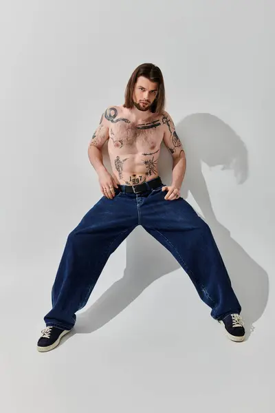 A man with a chest tattoo poses in front of a white wall. — Stock Photo