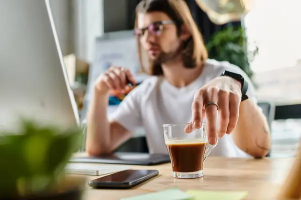Un uomo seduto a un tavolo, con un bicchiere di caffè in primo piano. — Foto stock