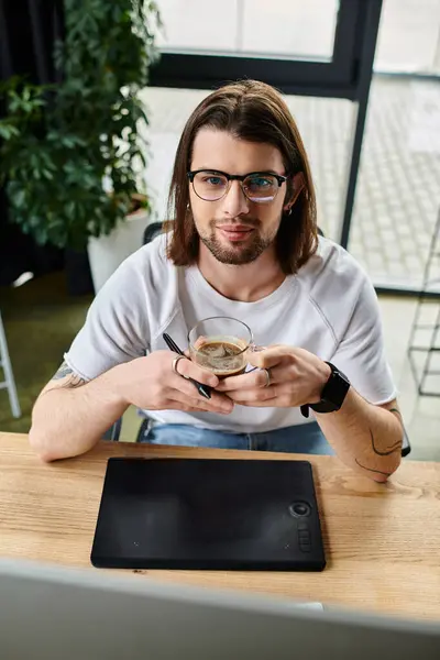 A caucasian man sits at a table holding a glass of coffee. — Stock Photo