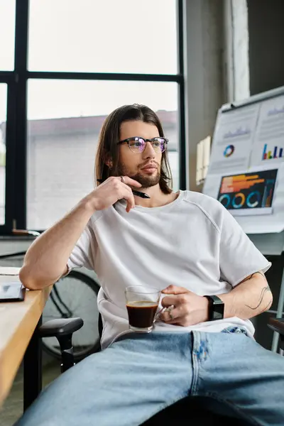 Um homem de negócios desfrutando de uma xícara de café enquanto trabalhava em sua mesa. — Fotografia de Stock