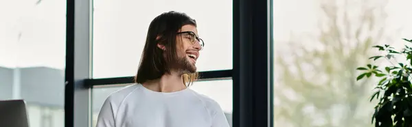 Handsome businessman with long hair stands contemplatively in front of a window. — Stock Photo