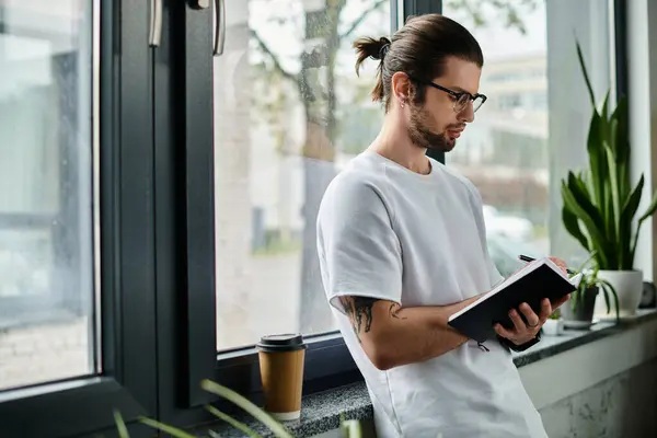 Un homme debout à une fenêtre, absorbé par la lecture d'un livre. — Photo de stock