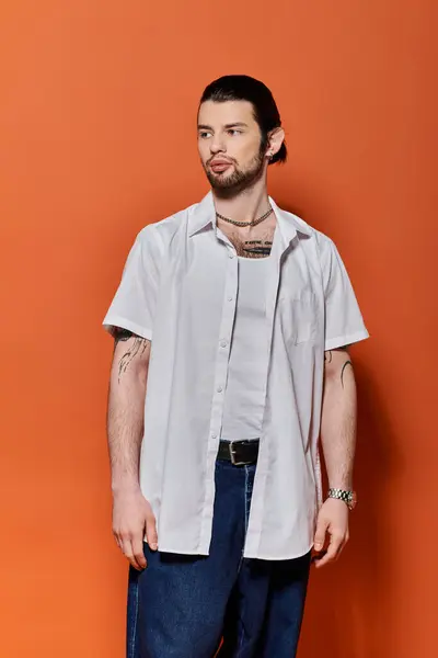 Stylish Caucasian man posing confidently in front of vibrant orange wall. — Stock Photo