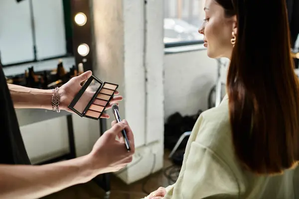 Un maquillador mejora las características de una cliente femenina con una aplicación hábil. - foto de stock