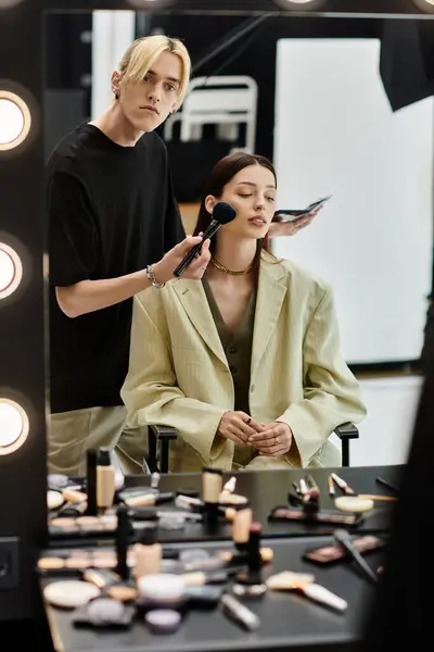 Frau sitzt am Spiegel und lässt sich von Künstlerin schminken. — Stockfoto