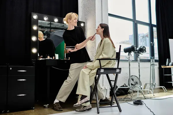 Женщина сидит перед зеркалом, как гример наносит макияж. — стоковое фото