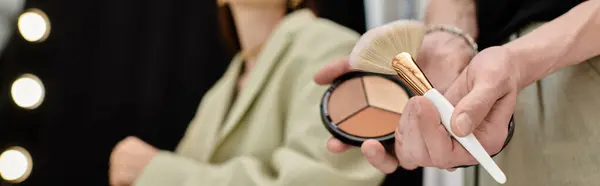 Primo piano di una persona che regge con grazia un pennello per il trucco, accanto al suo cliente. — Foto stock