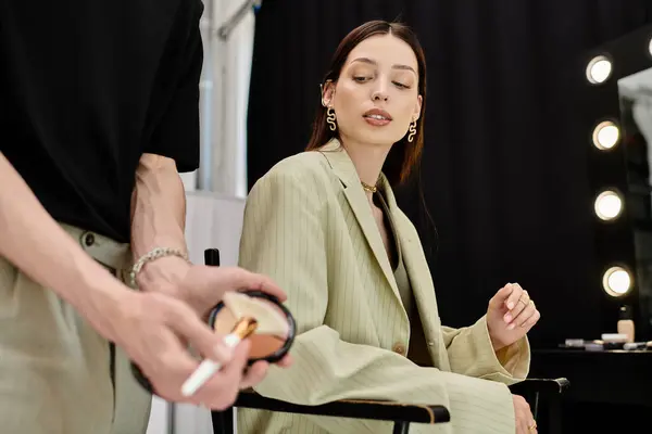 A woman sits in a chair, getting her makeup done in front of a mirror. — Stock Photo