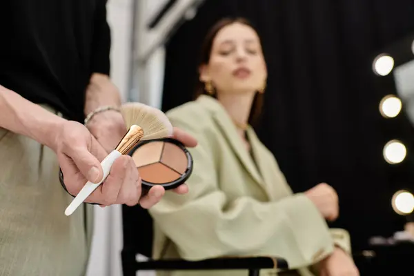 A woman sitting while a makeup artist applies makeup on her face. — Stock Photo