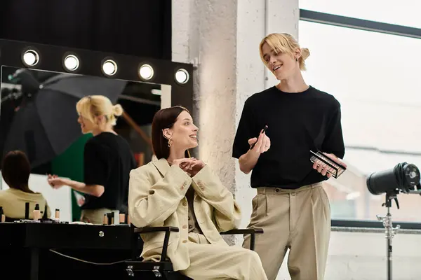Woman sits in chair as makeup artist applies makeup in front of mirror. — Stock Photo