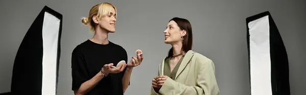 Un uomo applica il trucco su una donna di fronte a un muro grigio. — Foto stock