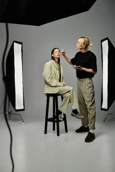 A woman sits on a stool, receiving makeup from a talented man. — Stock Photo